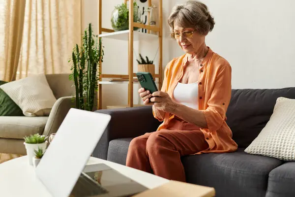Senior woman in comfy clothes relaxes on a couch while using her smartphone in a cozy living space. — Stock Photo