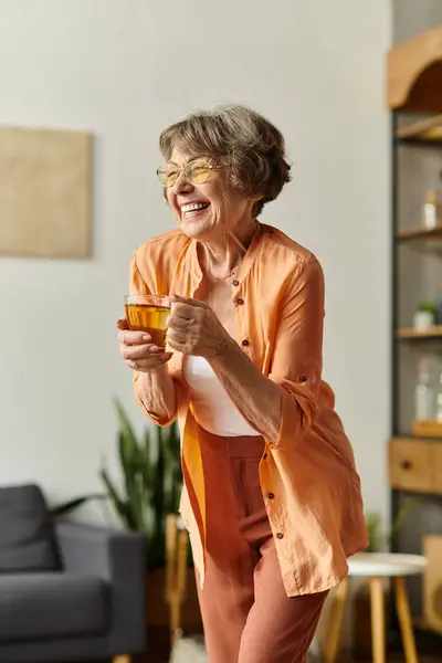 A senior woman with a warm smile savors her drink in a cozy, happy setting. — стоковое фото