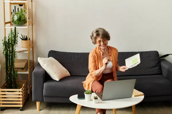 Warm atmosphere in a home as a senior woman smiles while taking notes and working on her laptop — Stock Photo