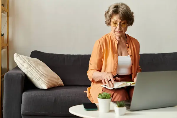 Senior woman relaxes in comfortable clothing while reading and working on her laptop at home. — Stock Photo