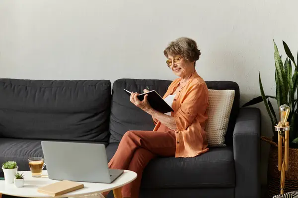Senior woman relaxes at home, writing in her journal while sipping tea in a cozy setting. — Stock Photo