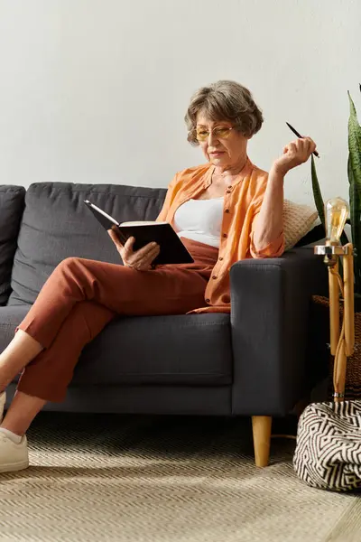 Mature woman relaxes on her couch, reading a book while embracing the cozy atmosphere of home. — Stock Photo