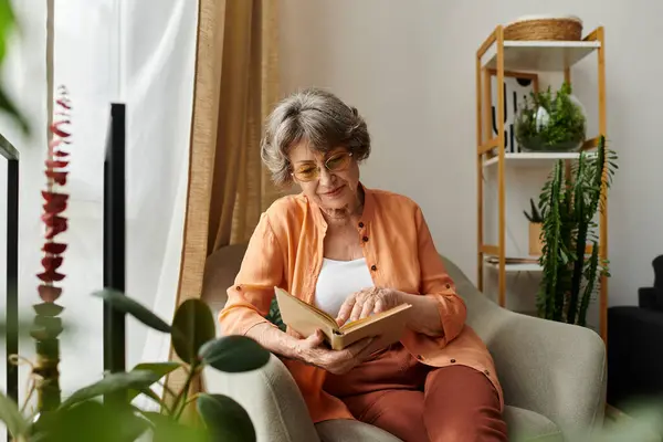 Senior woman in cozy attire reads a book in her serene home environment, surrounded by plants. — Stock Photo