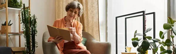Senior woman relaxes with her favorite book in a cozy, plant filled living room. — Stock Photo