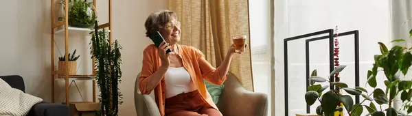 A senior woman relaxes on her couch with a drink, happily chatting on the phone. — Stock Photo