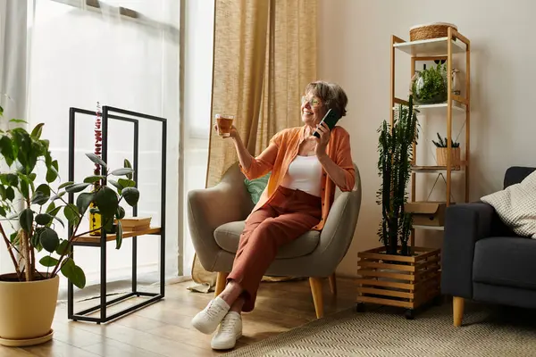 Senior woman relaxes in a comfy chair, sipping a drink and enjoying a peaceful moment indoors. — Stock Photo
