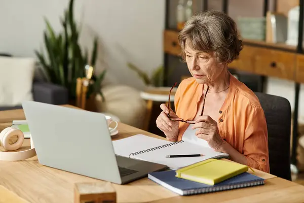 Mature woman sits comfortably in her home, working intently at her desk with a laptop. — Stock Photo