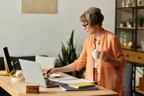 Senior woman in cozy attire engages in creativity at home while sipping tea and taking notes. — Stock Photo