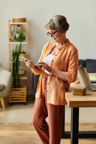 Senior woman dressed in cozy attire engages with her tablet in a warm and inviting living space. — Stock Photo