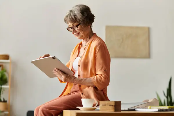 Donna matura in abbigliamento accogliente utilizza un tablet mentre rilassarsi comodamente a casa. — Foto stock