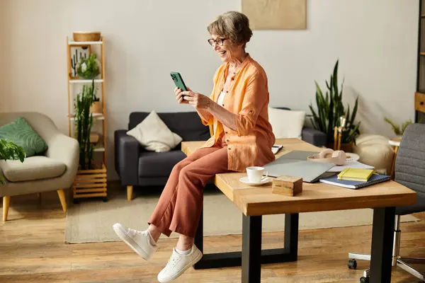 A senior woman in comfy clothes smiles while using her smartphone at home. — Stock Photo