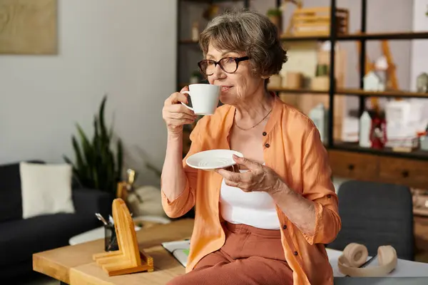 Mature woman savors a warm cup of tea, enveloped in comfort within her stylish living space. — Stock Photo