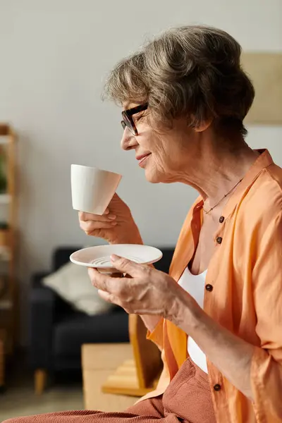 Mature woman sips a warm beverage at home, embracing comfort and tranquility in her surroundings. — стоковое фото
