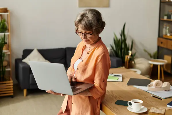 A senior woman uses her laptop in a cozy, plant filled living room. — Stock Photo