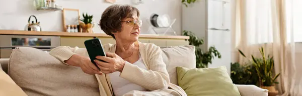 Senior woman relaxes in a cozy living room while browsing on her smartphone. — Stock Photo