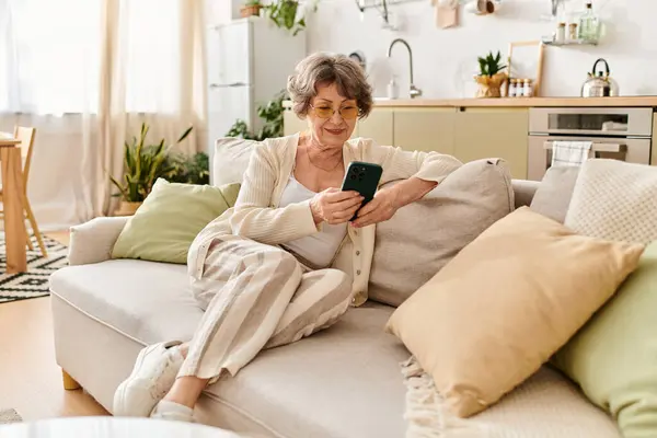In a cozy living room, a mature woman relaxes on her couch, engaged with her smartphone. — Stock Photo