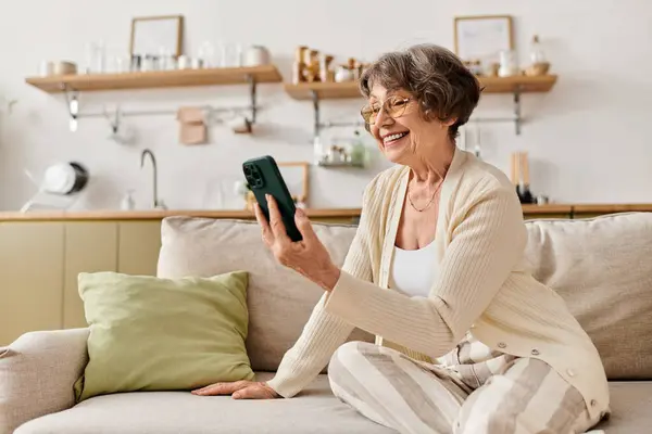 A relaxed woman smiles at home while connecting with family on her phone. — Stock Photo