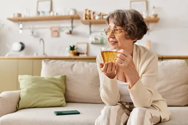 Senior woman enjoys a warm beverage while relaxing comfortably at home in cozy attire. — Stock Photo