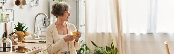Frau in kuscheliger Kleidung genießt Tee in ihrem einladenden, gut beleuchteten Haus. — Stockfoto