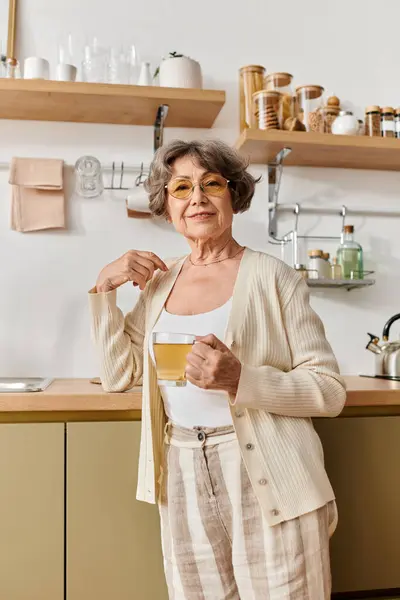 A senior woman dressed in cozy attire relaxes at home while sipping tea, radiating comfort. — Stock Photo