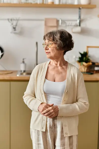 A mature woman in cozy clothing stands thoughtfully in her stylish kitchen, enjoying home life. — Stock Photo