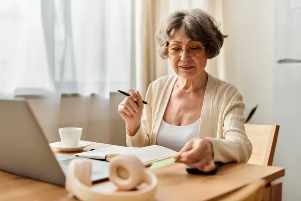 Mature woman in comfortable attire engaging with her laptop and notebook at home — Stock Photo