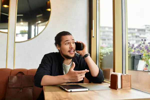 Young man with a beard enjoys a busy day working remotely while conversing on the phone in a cafe. — Stock Photo