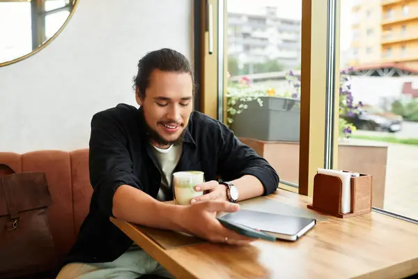 A young man with a beard relaxes in a cafe, sipping matcha — Stock Photo