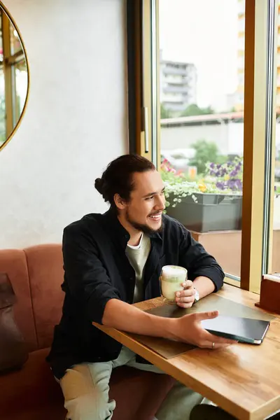 Young man with a beard smiles while sipping matcha in a cozy cafe. — Stock Photo