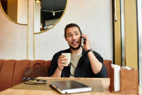 A young man with a beard talks on the phone while savoring his matcha at a cozy cafe. — Stock Photo