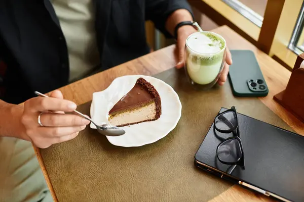 Young man sips matcha and takes a bite of cake in a cafe. — Stock Photo