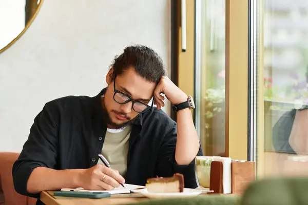 Young man enjoys working remotely in a cafe, savoring matcha and cake while writing notes. — Stock Photo
