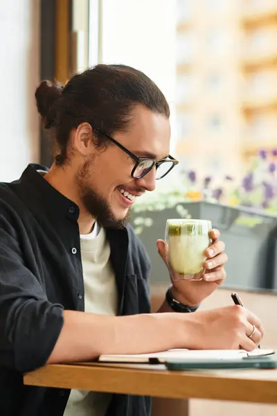 Cheerful man savors matcha and taking notes at a cafe on a sunny day. — стоковое фото