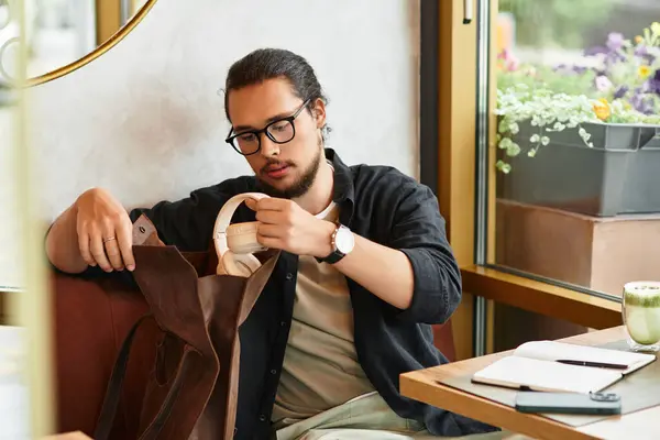 Young man with a beard taking headphones from his bag in a cafe. — Stock Photo