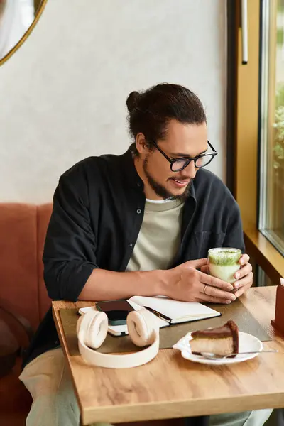 A young man with a beard savors matcha and cake in a charming cafe. — Stock Photo