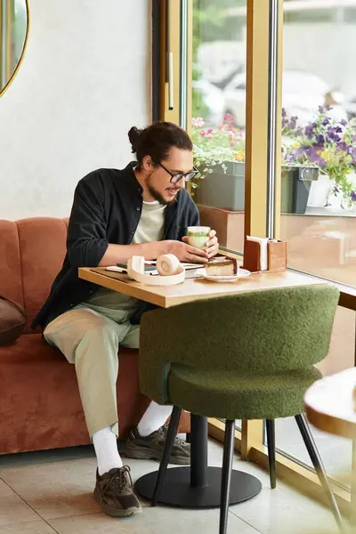 A young man enjoys his matcha and cake while working in a bright cafe. — Stock Photo