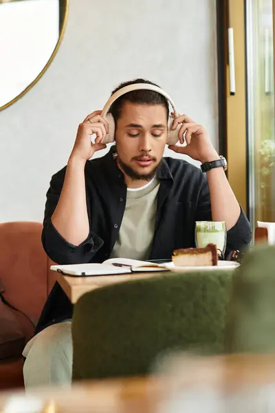 A young man with a beard listens to music, absorbed in work while savoring matcha and cake. — Stock Photo
