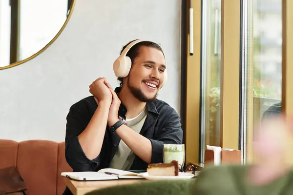 A young man with a beard enjoying food and drink while focused on tasks. — Stock Photo
