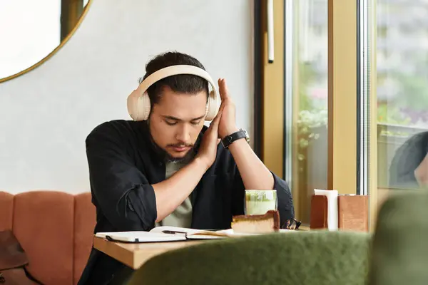 A young man with a beard focuses on his work, sipping matcha and enjoying cake in a cafe. — Stock Photo