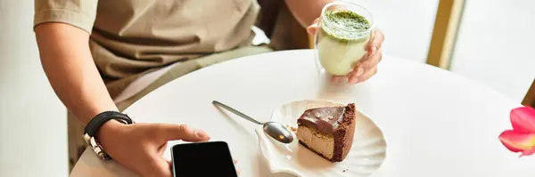 A young man focuses on his phone at a cafe, sipping matcha and enjoying dessert. — Stock Photo