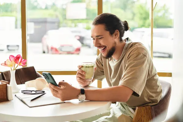 Working remotely in a cozy cafe, a young man shares a joyful moment while sipping matcha. — Stock Photo