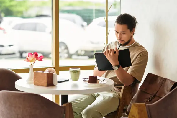 Young man with a beard focuses on work while enjoying matcha and cake in a cafe. — Stock Photo