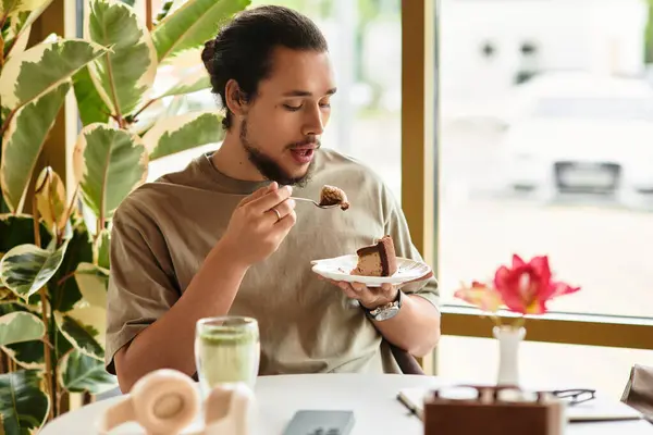 A young man with a beard savoring cake and matcha in a cozy cafe. — Stock Photo