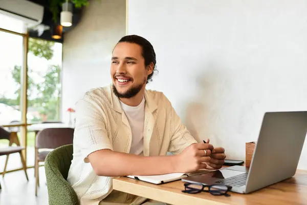 Young man with a beard happily works remotely in a vibrant cafe, enjoying the summer atmosphere. — Stock Photo
