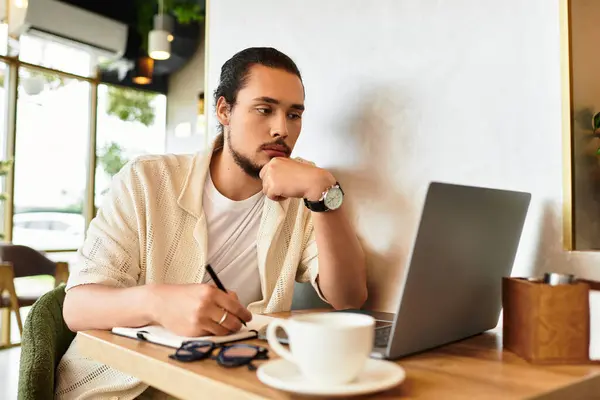 A focused young man with a beard types on his laptop at a busy cafe, sipping coffee. — Stock Photo