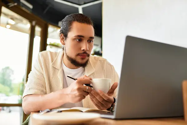 Young man sips coffee and works on his laptop in a vibrant cafe on a sunny summer day. — Stock Photo