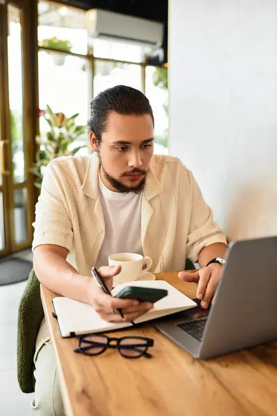 A young man with a beard works diligently on his laptop while sipping coffee in a warm cafe. — Stock Photo