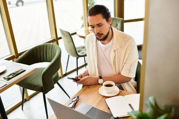 A young man with a beard is focused on remote work at a cozy cafe while sipping coffee. — Stock Photo