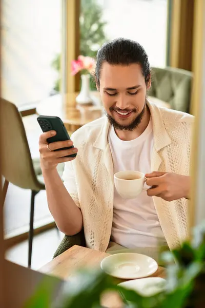 Freelancer relaxes in a cafe, sipping coffee and engaging with his phone while working. — Stock Photo