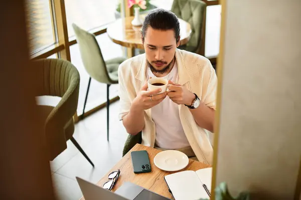 A young man sips coffee as he engages in remote work at a stylish cafe on a summer day. — Stock Photo
